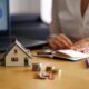 Mulher ao lado de miniatura de casa e moedas, representando o consórcio para quitar financiamento imobiliário