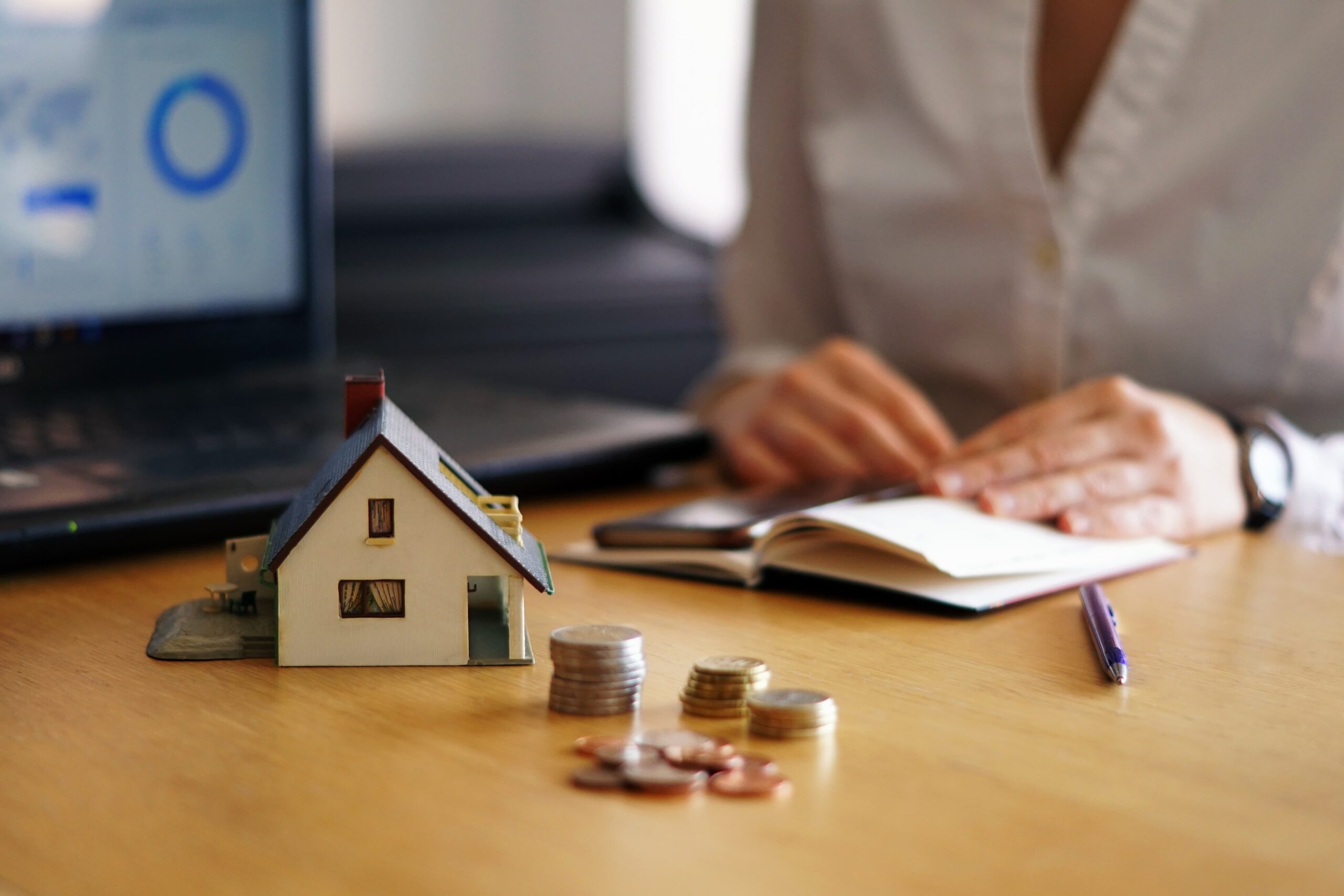 Mulher ao lado de miniatura de casa e moedas, representando o consórcio para quitar financiamento imobiliário